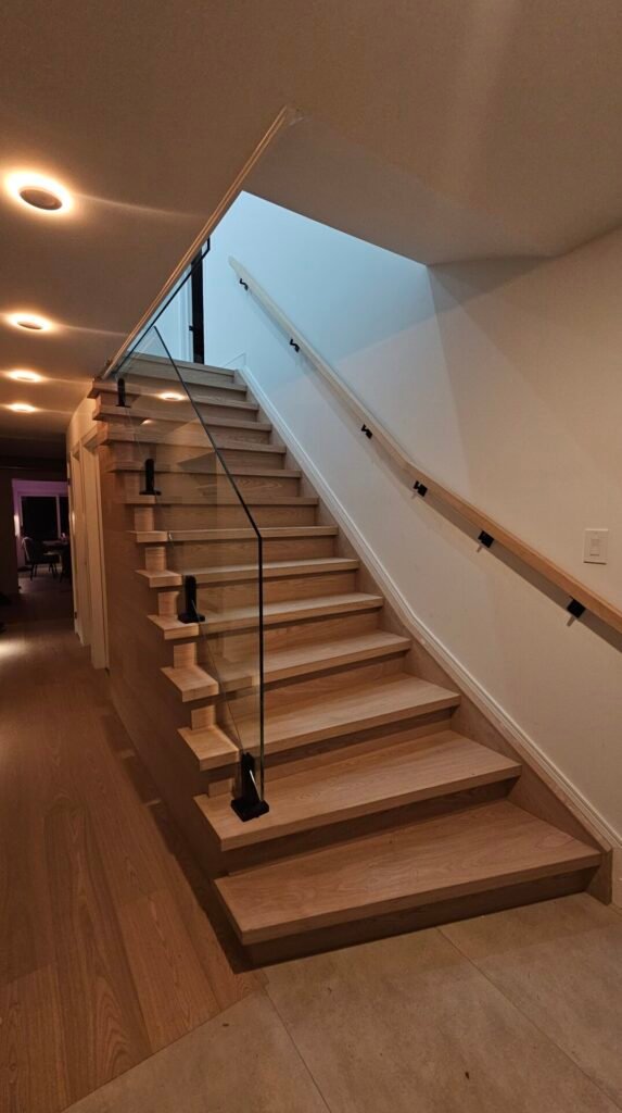 Interior glass railings with black spigots and a wooden handrail